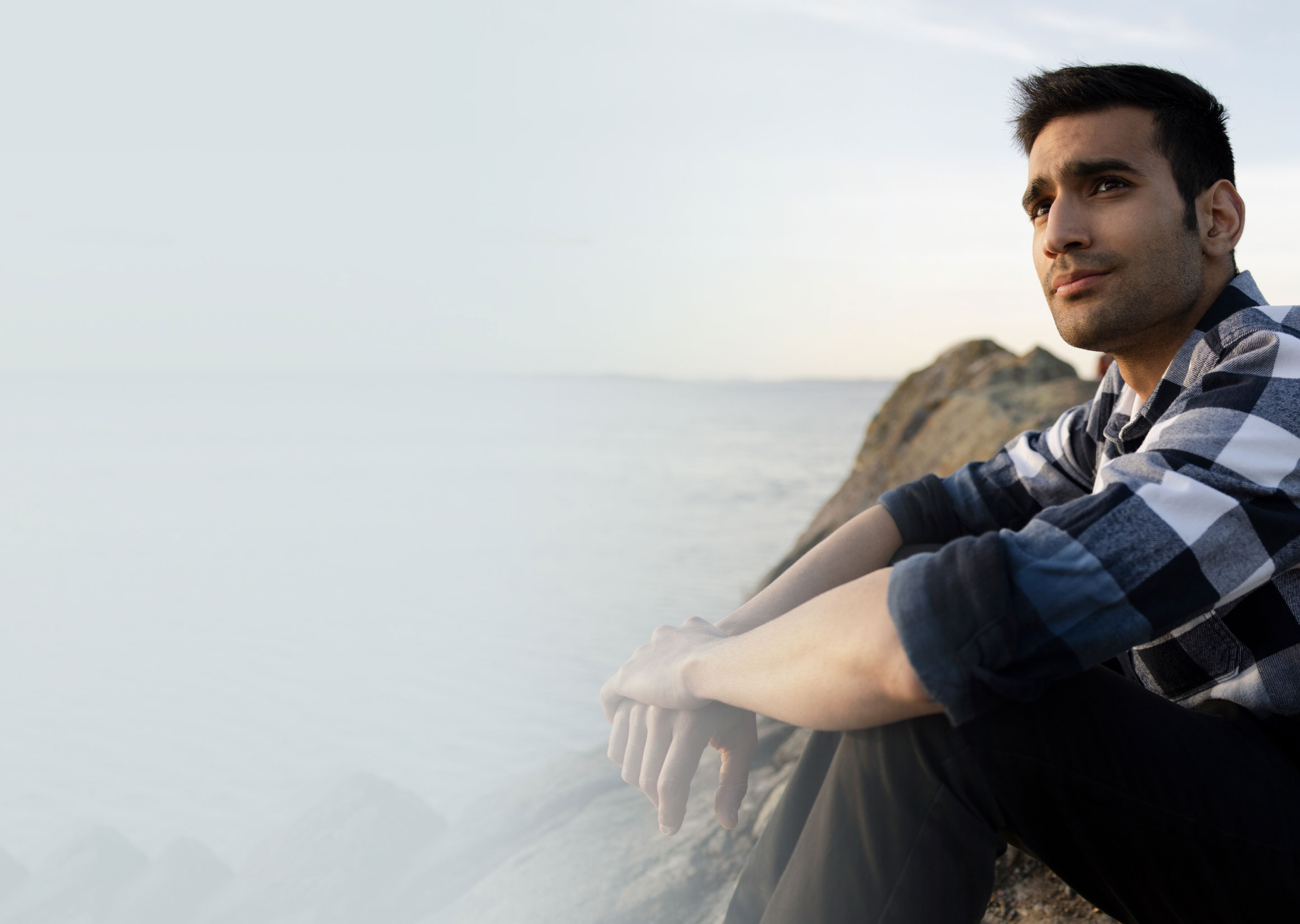 man sitting on some rocks by the water